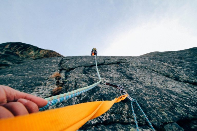 Pullback trading strategy concept: a rock climber roped and clipped to protection while ascending a granite face