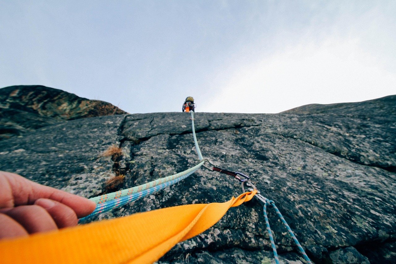 Pullback trading strategy concept: a rock climber roped and clipped to protection while ascending a granite face