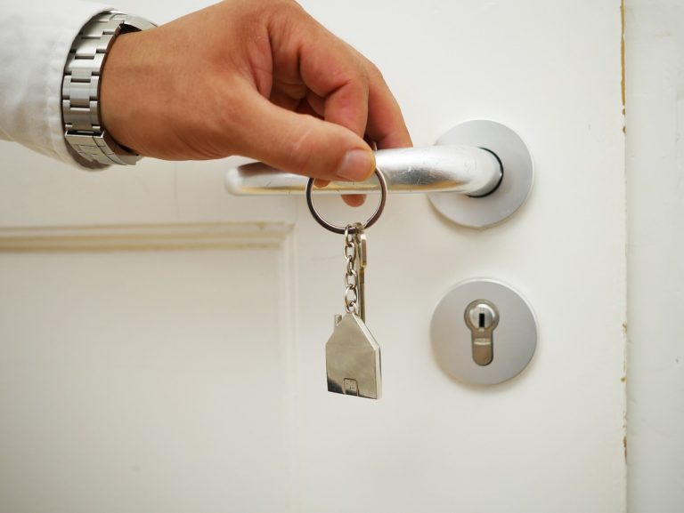 Aavas Financiers Q2 results: a hand holding a house-shaped key ring next to a white front door