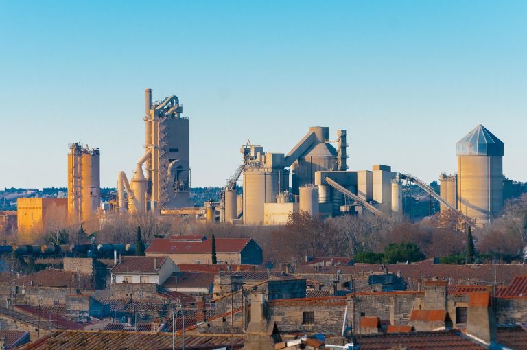 Ambuja Cements Q2 results: cement plant with silos and kiln towers above town rooftops