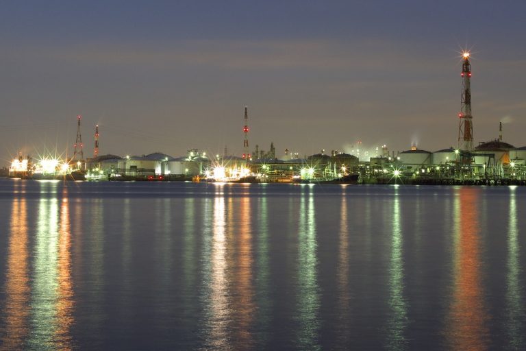 Atul Q2 results: a chemical plant lit up at dusk with storage tanks and towers reflected in the water