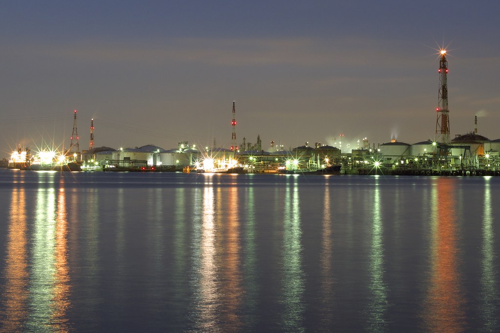 Atul Q2 results: a chemical plant lit up at dusk with storage tanks and towers reflected in the water