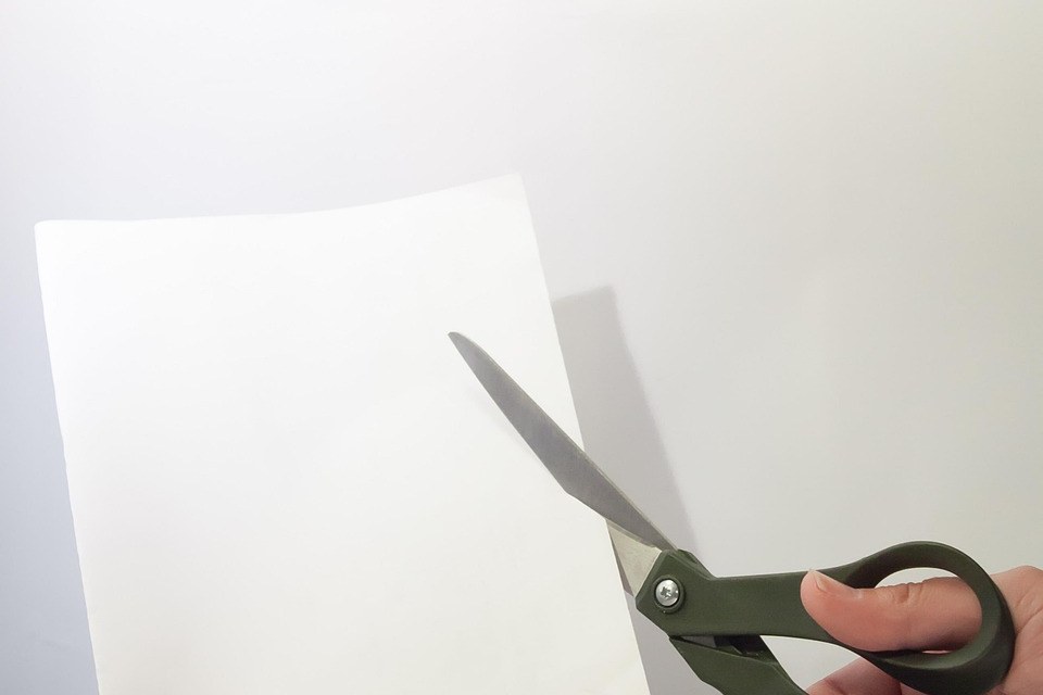 Capital reduction of shares: a hand cutting a sheet of paper with scissors