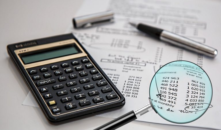 CARO report review: a magnifying glass over figures on an audit worksheet beside a calculator