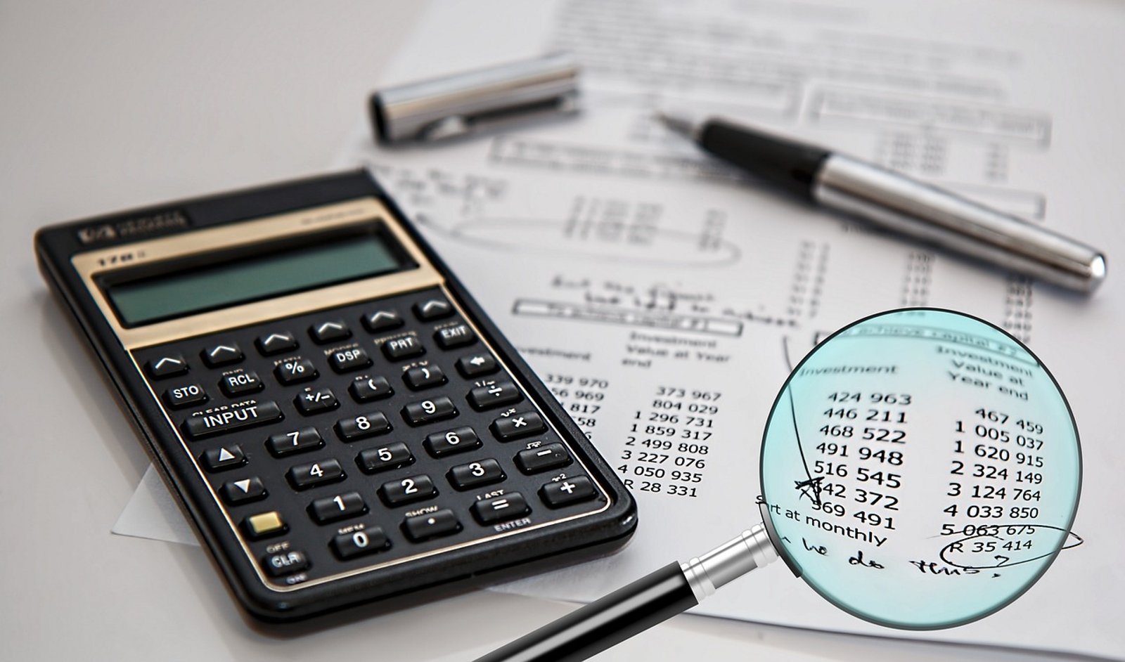CARO report review: a magnifying glass over figures on an audit worksheet beside a calculator