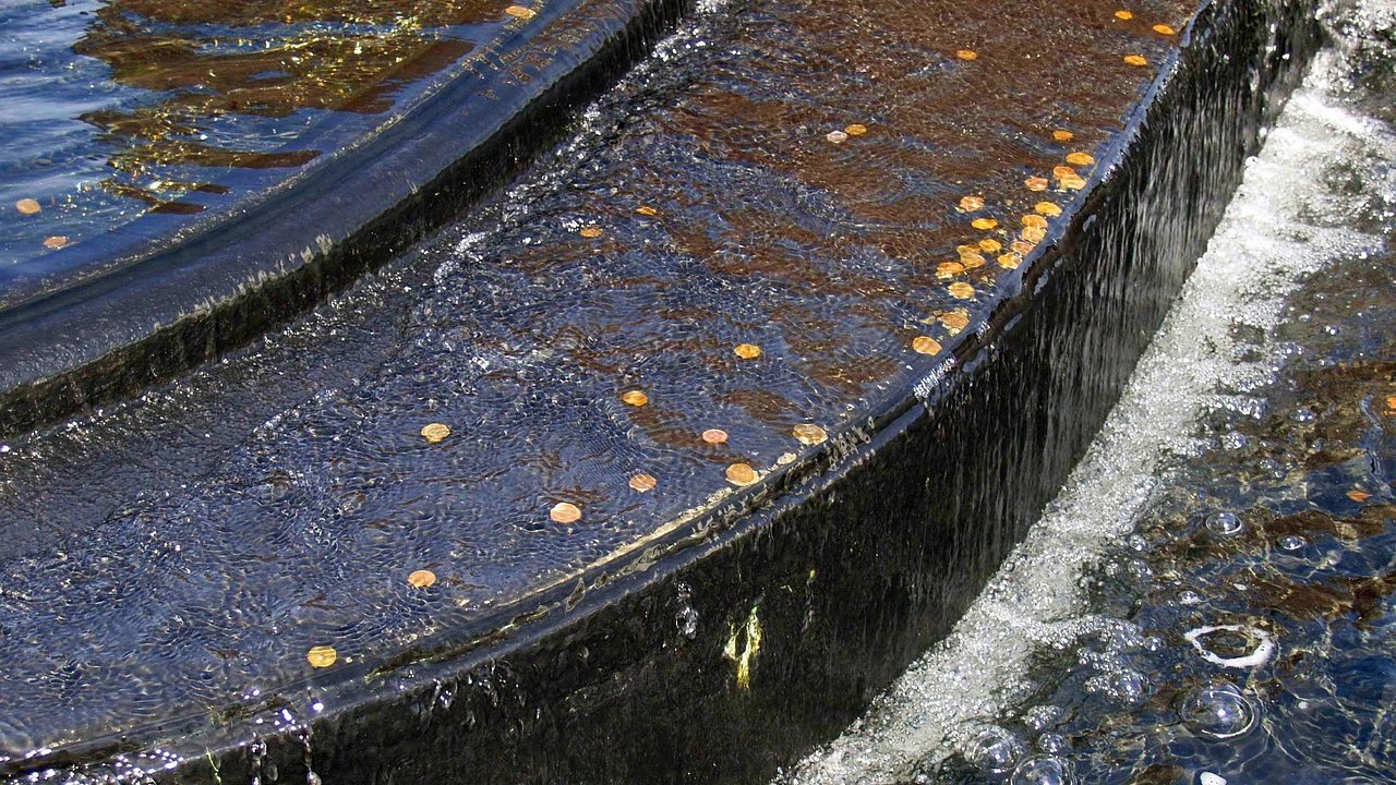 Chaikin money flow indicator: water spilling over the rim of a fountain basin scattered with coins