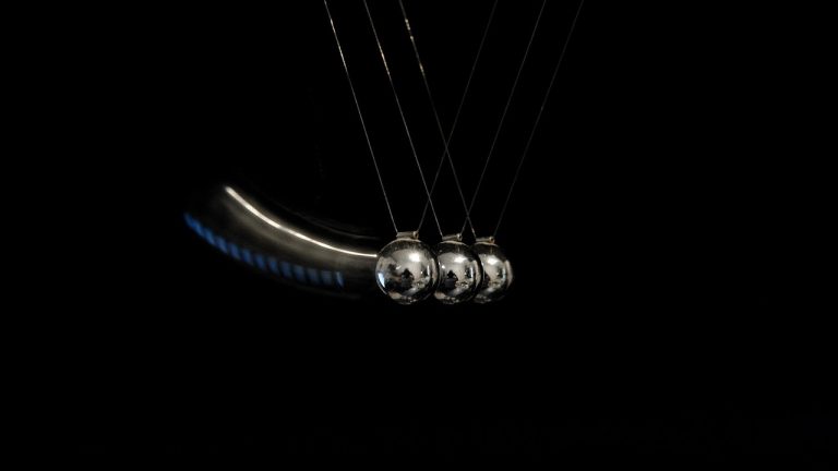 Commodity channel index concept: Newton's cradle steel balls swinging against a black background
