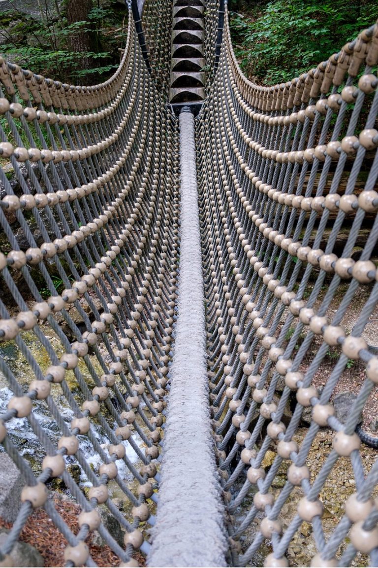Credit risk fund concept: a narrow rope bridge across a forest stream, a reminder that higher-yield debt comes with a shakier crossing