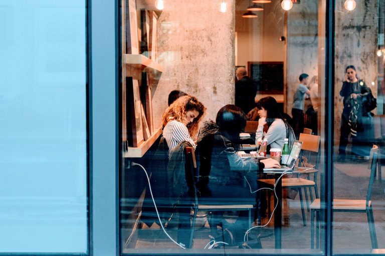 Employee cost in quarterly results: employees working on laptops at a shared table seen through an office window