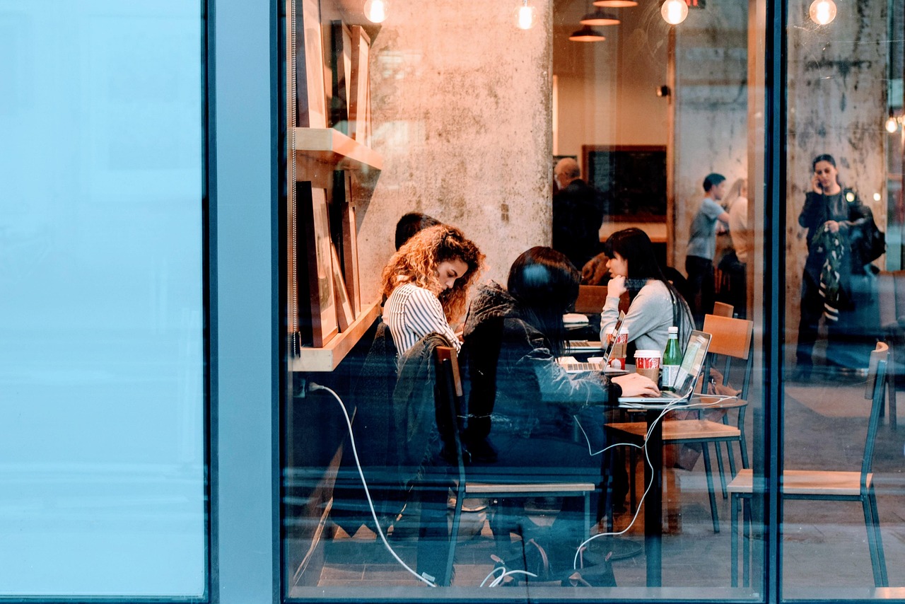 Employee cost in quarterly results: employees working on laptops at a shared table seen through an office window