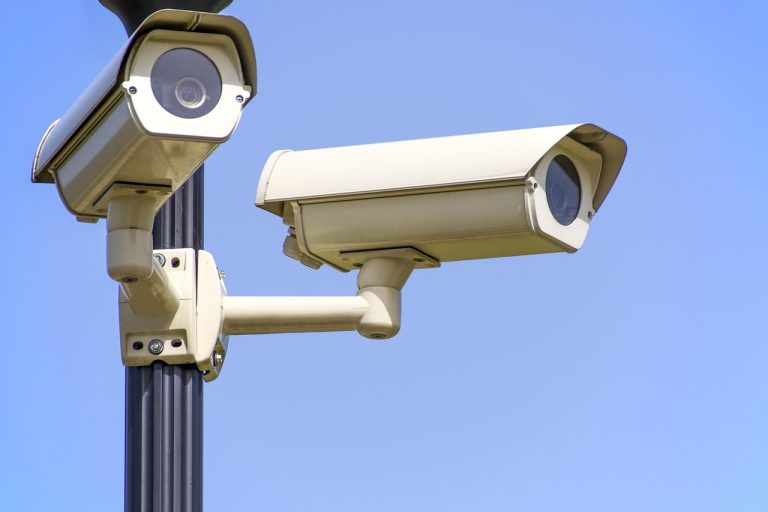 Enhanced surveillance measure ESM: two white CCTV surveillance cameras on a pole against a clear blue sky