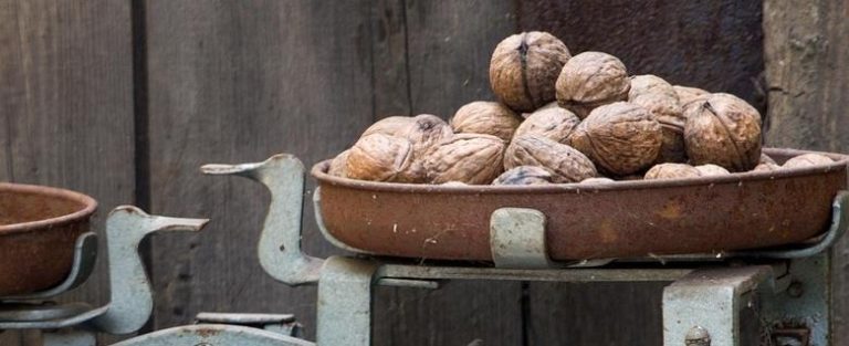 ETF indicative NAV: an old metal weighing scale with a rusty pan piled with walnuts against a weathered wooden wall