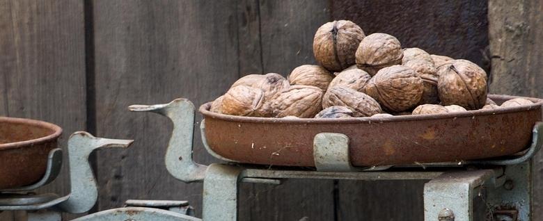 ETF indicative NAV: an old metal weighing scale with a rusty pan piled with walnuts against a weathered wooden wall
