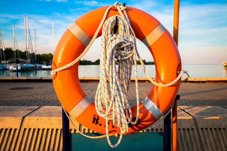 Extreme loss margin: an orange lifebuoy with coiled rope hanging on a lakeside pier at sunset