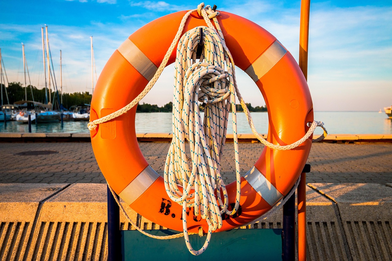Extreme loss margin: an orange lifebuoy with coiled rope hanging on a lakeside pier at sunset