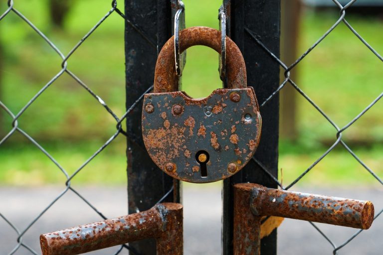F&O ban list NSE: a rusty padlock locking a metal gate in a chain-link fence