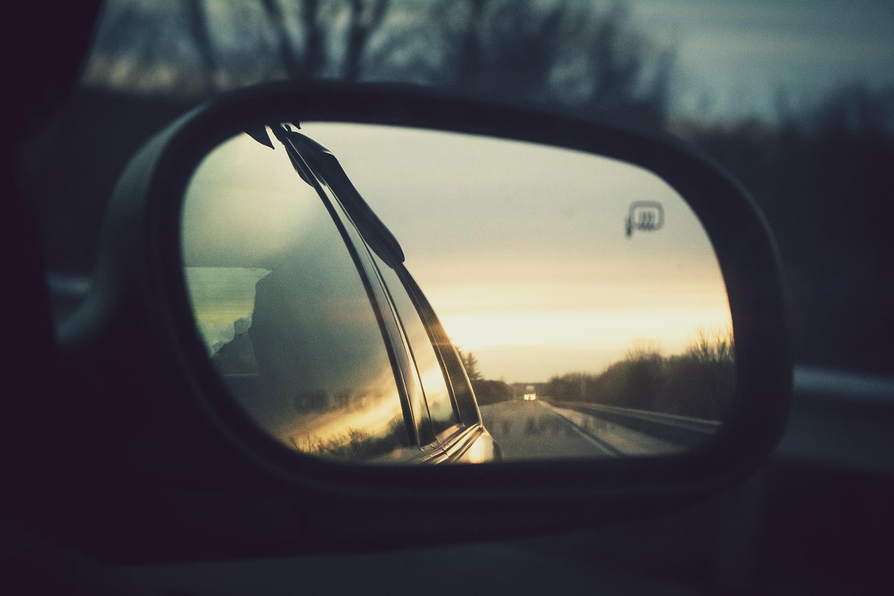 Hindsight bias in trading: a car rear-view mirror reflecting the road already travelled at dusk