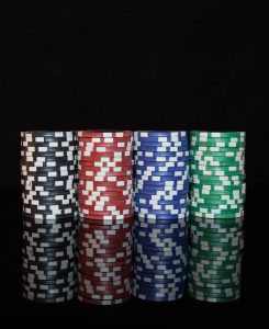 House money effect concept: four stacks of poker chips in black, red, blue and green on a dark reflective table