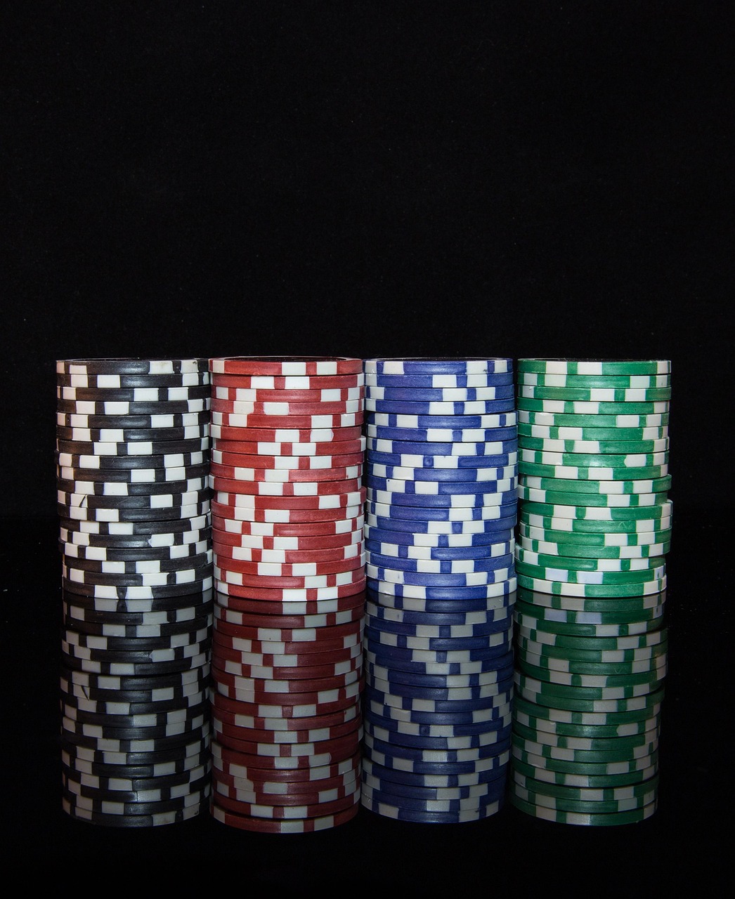 House money effect concept: four stacks of poker chips in black, red, blue and green on a dark reflective table