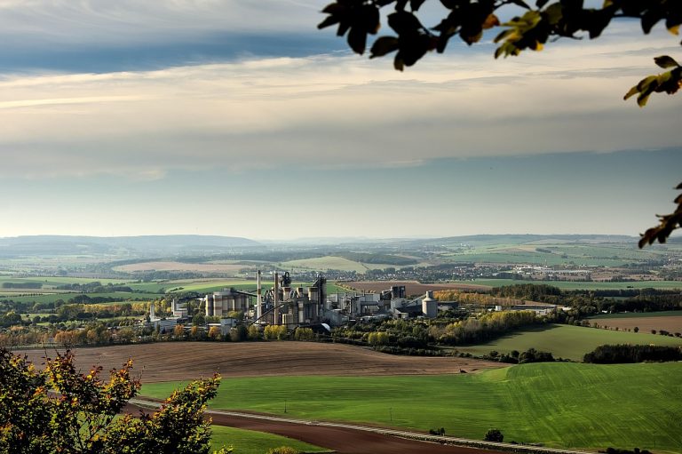 JK Cement Q2 results: a cement plant with silos and a kiln tower set among green farm fields