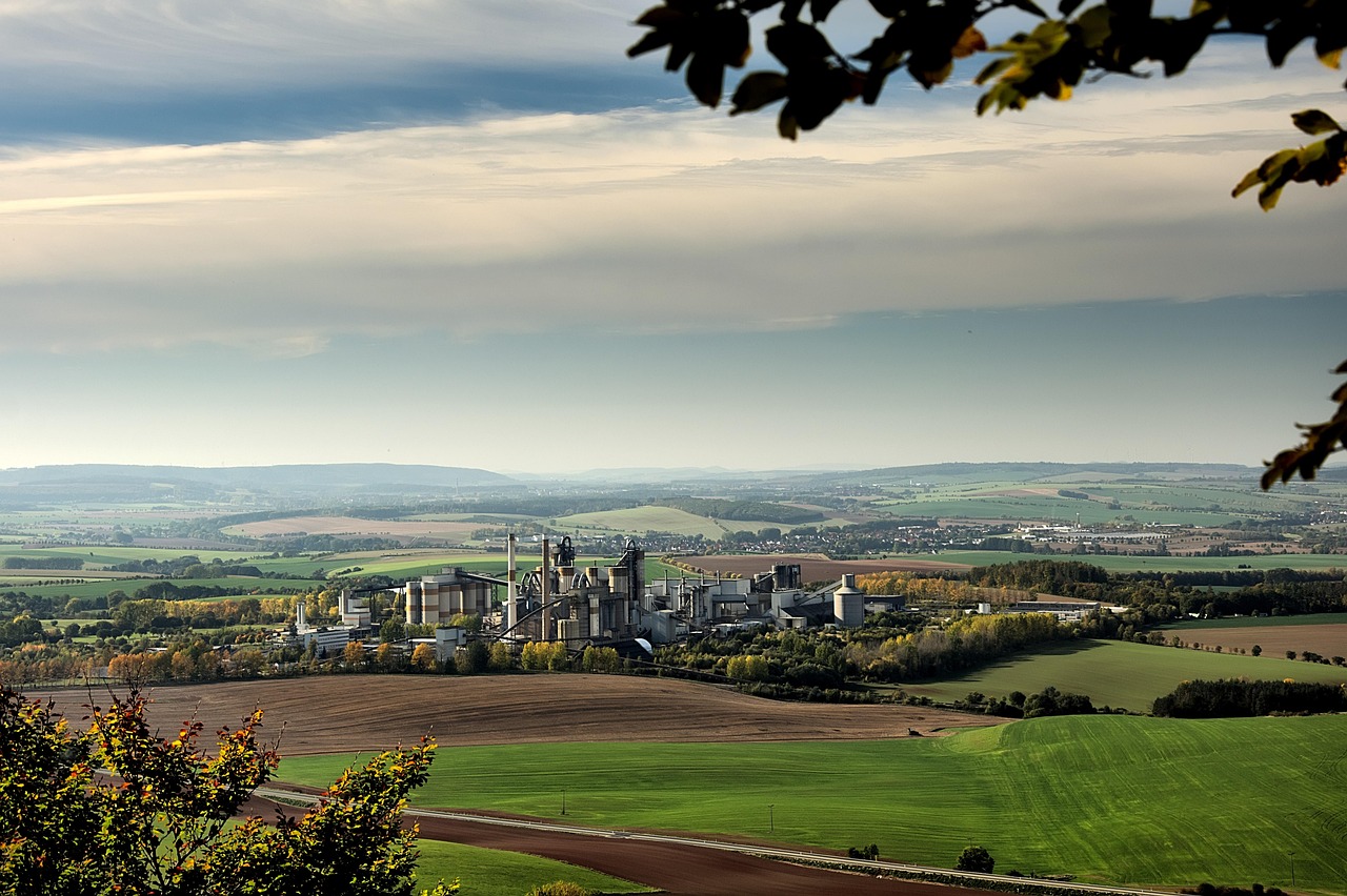 JK Cement Q2 results: a cement plant with silos and a kiln tower set among green farm fields