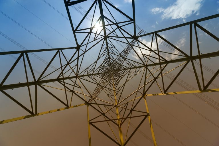 KEC International PGCIL order: looking up through the steel lattice of a high-voltage transmission tower against a blue sky