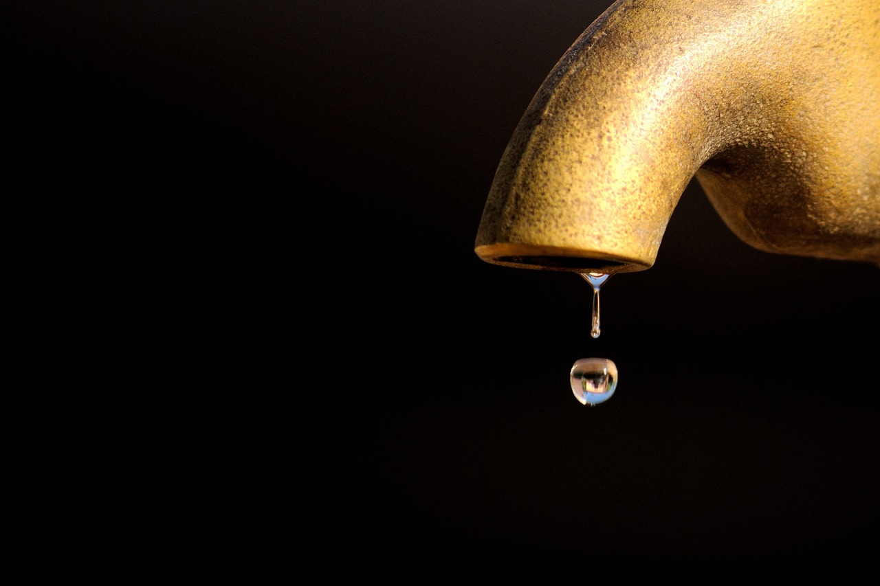 Mutual fund expense ratio concept: a single drop of water falling from a brass tap, like a small fee leaving a fund every day