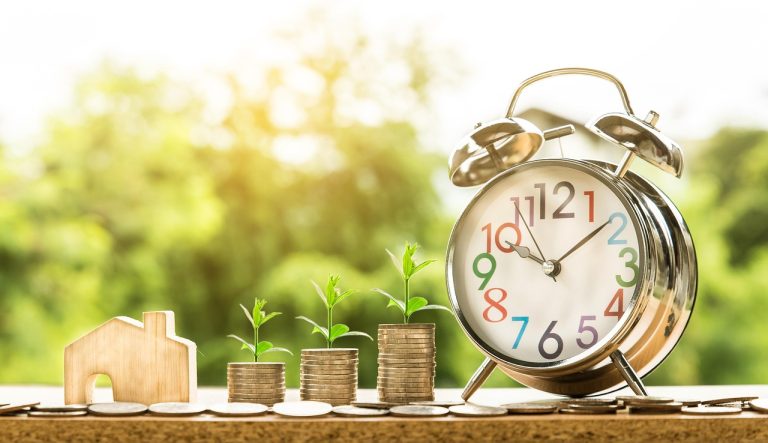 PEG ratio: stacks of coins with seedlings growing on them beside an alarm clock, a picture of earnings growth over time