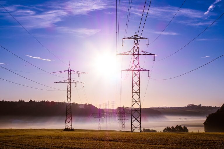 CPSE ETF idea: electricity pylons and power lines across a misty field at sunrise