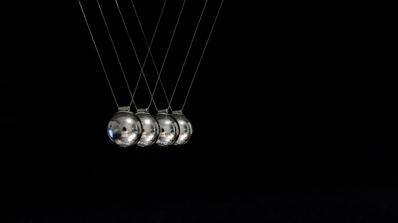 Awesome oscillator momentum concept: a Newton's cradle with steel balls swinging against a dark background