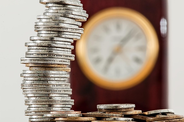 Yield to maturity concept: a tall stack of coins in front of a blurred wall clock, showing money growing over time
