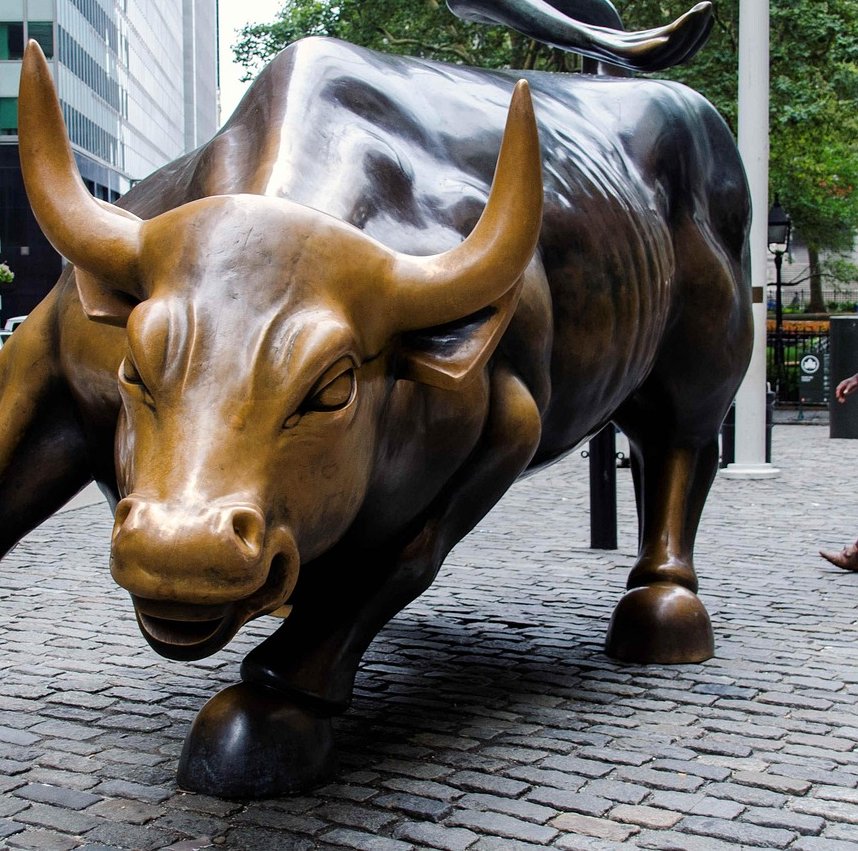 Bull put spread concept: a bronze charging bull statue on a cobbled street, a symbol of a mildly bullish market view
