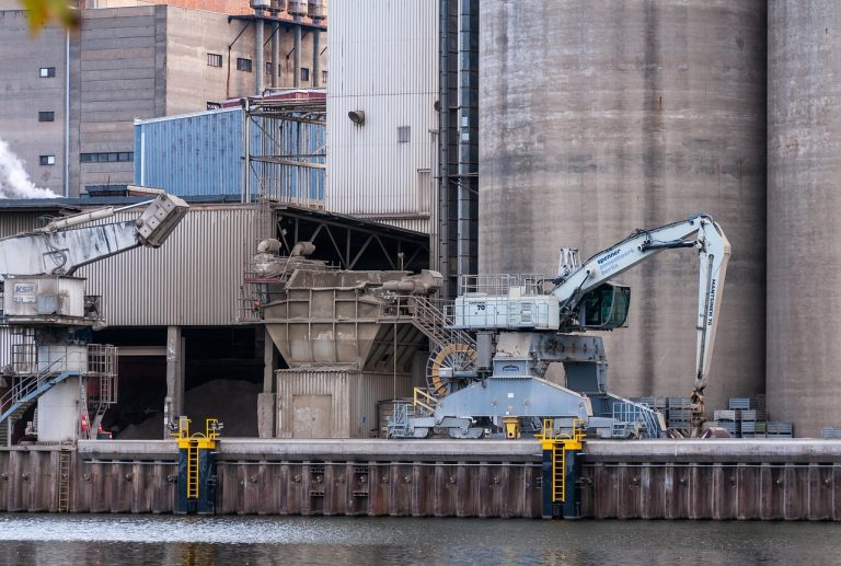 India Cements Q2 results: tall concrete cement silos and a loading crane at a riverside cement plant