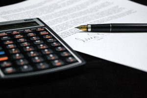 IPO issue expenses: calculator, fountain pen and a signed agreement on a desk