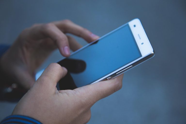 Just Dial Q2 results: two hands typing on a white smartphone against a dark blue background