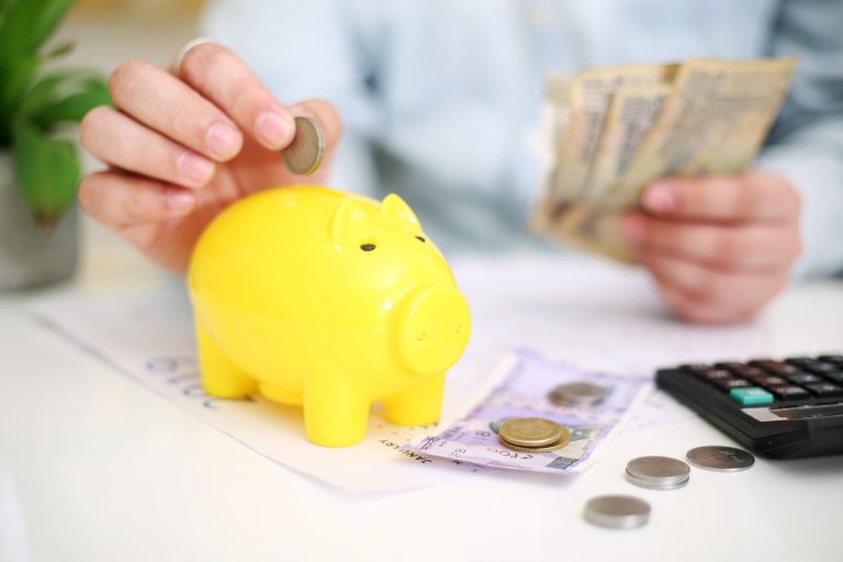 Listing gains tax India: hands counting rupee notes beside a yellow piggy bank and a calculator