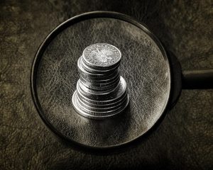 Magic formula investing: a magnifying glass held over a stack of coins on a dark leather surface