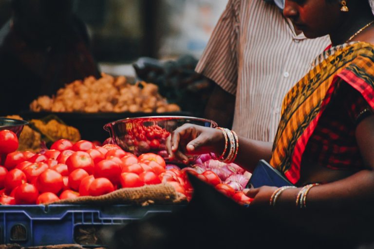 Market depth trading: a buyer picks tomatoes at a busy Indian vegetable stall while the seller waits beside the produce