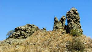 Matching low pattern concept: two weathered rock pillars of similar height standing side by side on a dry hillside under a clear blue sky