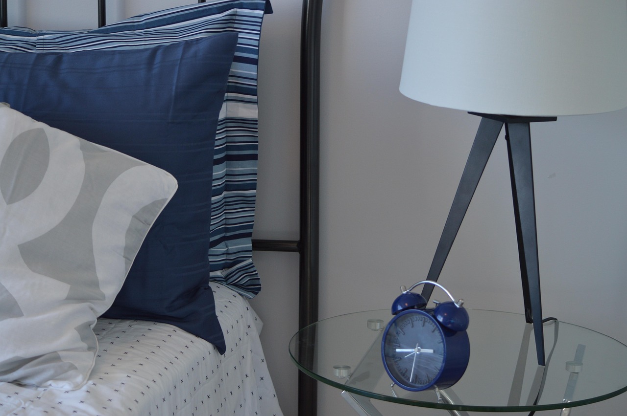 Overnight fund concept: a blue alarm clock on a glass bedside table next to a bed and lamp
