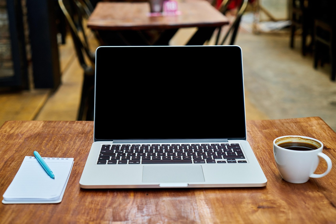 Rolling options positions: a laptop, notepad and coffee on a trader's desk before planning the next expiry