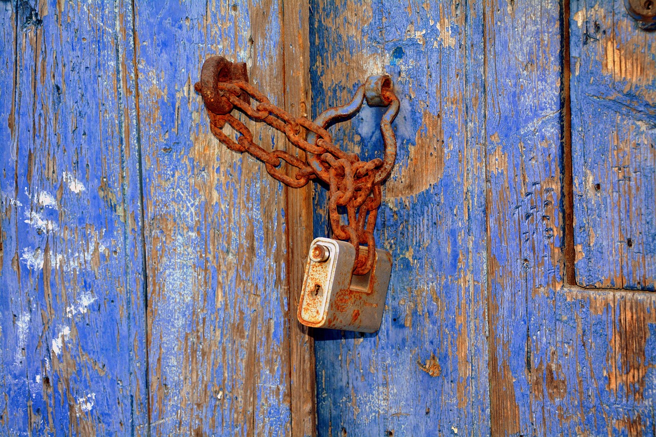 Promoter pledge meaning: a rusty chain and padlock holding shut an old blue wooden door