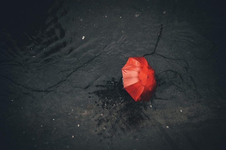 Protective put strategy: a red umbrella lying open on a wet, dark pavement in the rain
