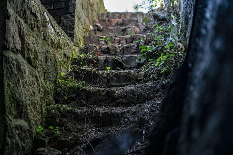 Rising wedge pattern concept: old stone stairs climbing upward through a narrowing passage between mossy walls