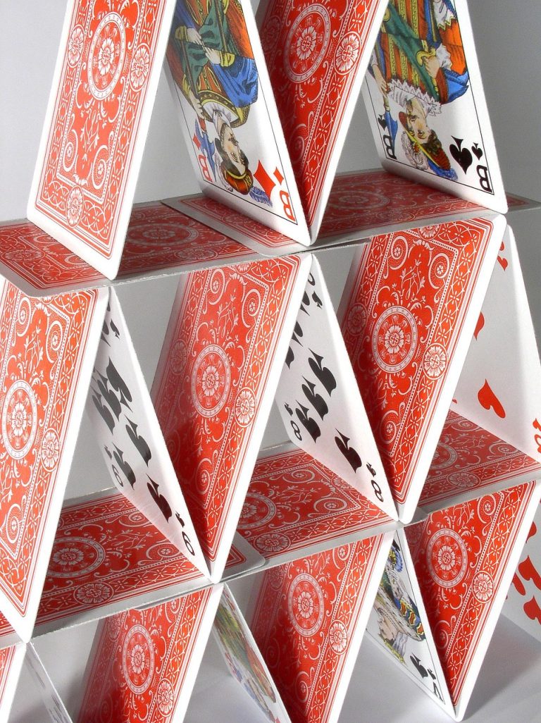 Risk of ruin concept: a tall, fragile house of playing cards with red patterned backs stacked in several levels