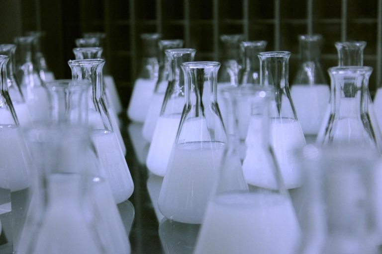 Rossari Biotech Q2 results: rows of glass laboratory flasks filled with white liquid on a lab bench