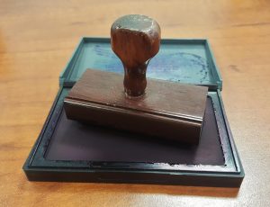 Secretarial audit report: a wooden rubber stamp resting on an ink pad on an office desk