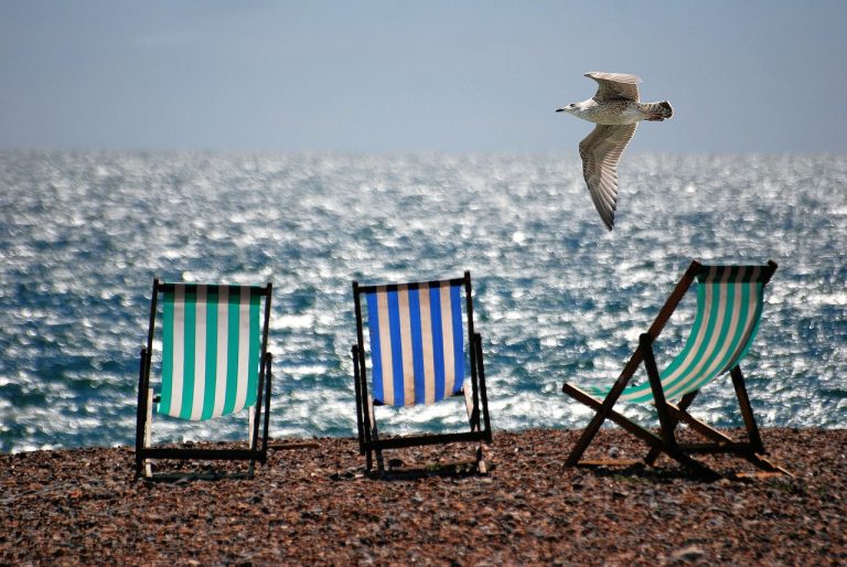 Sell in May and go away: empty striped deckchairs on a pebble beach by a sunlit sea