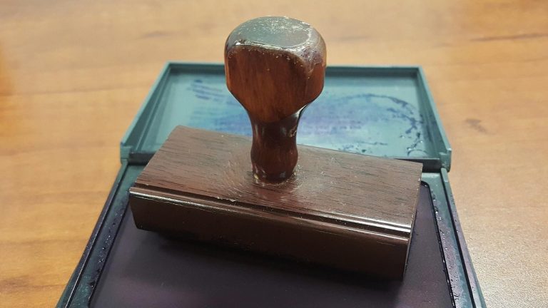 Stamp duty on share transactions: a wooden rubber stamp resting on an open ink pad on an office desk