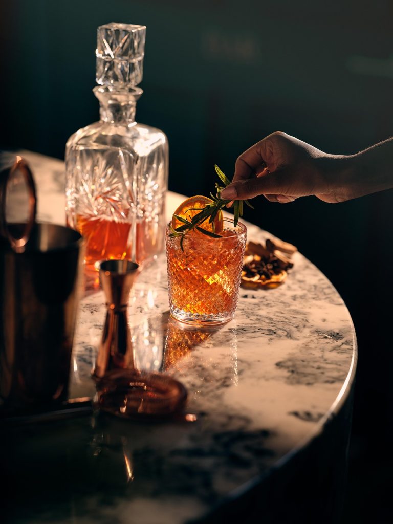United Spirits Q2 results: crystal whisky decanter and a garnished drink on a marble bar table